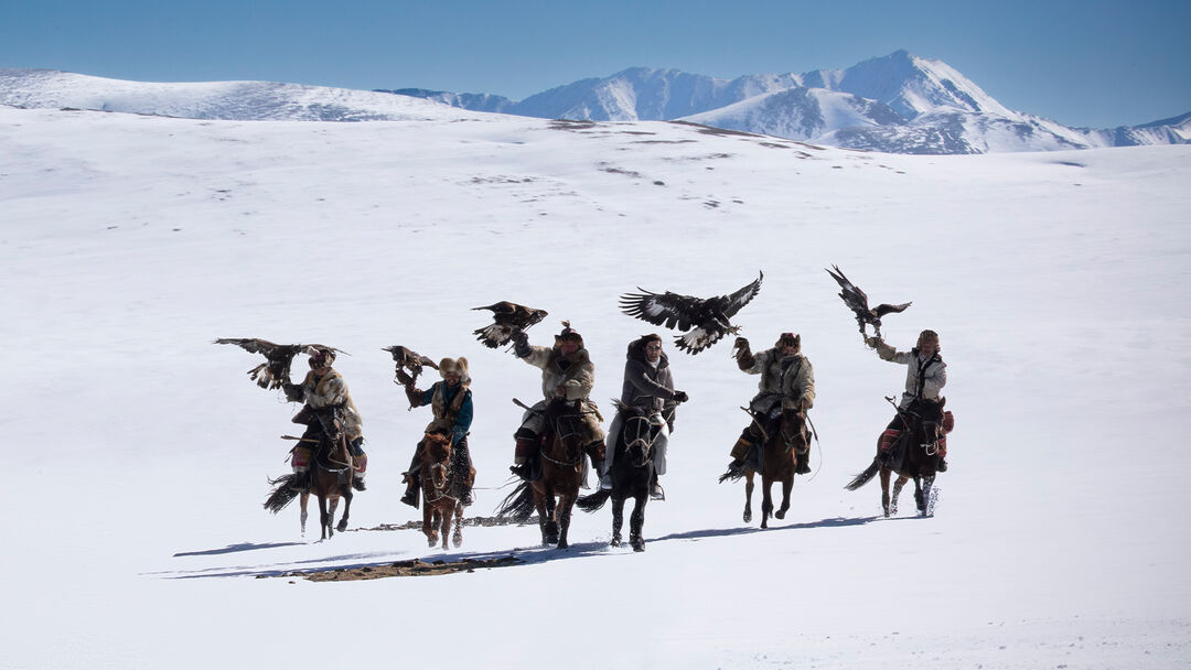 men riding horses in the snow in Mongolia