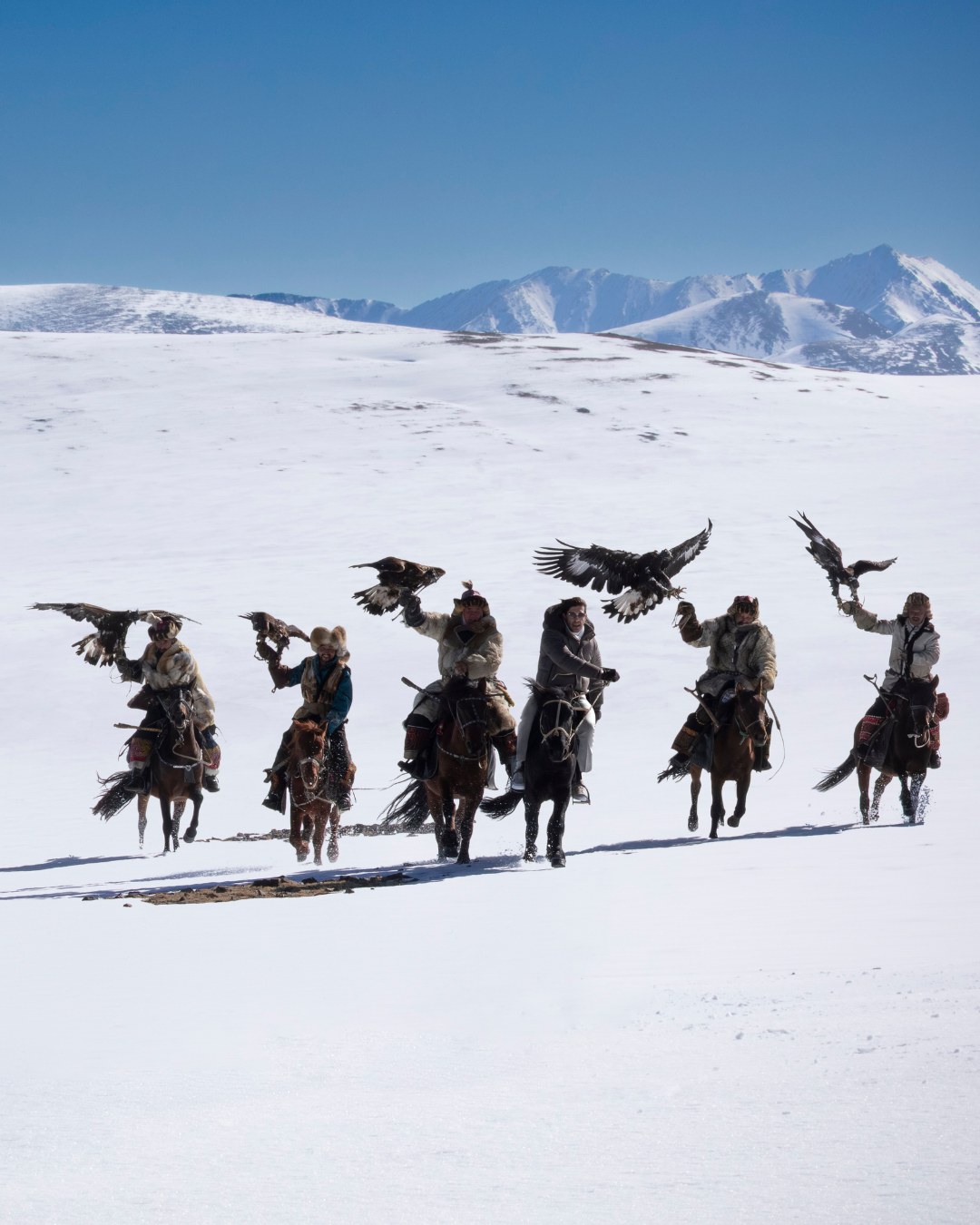 men riding horses in the snow in Mongolia
