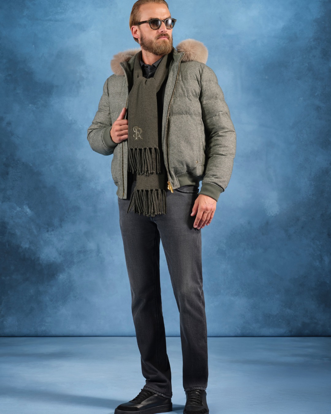 The model wears a hooded down jacket in a luxurious wool, silk, and cashmere blend, adorned with a fox fur trim, paired with a soft cotton and silk jersey shirt and SR jeans.